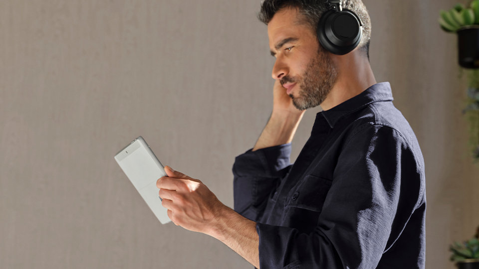 A person holding Surface Go 3 for Business and wearing Surface Headphones.