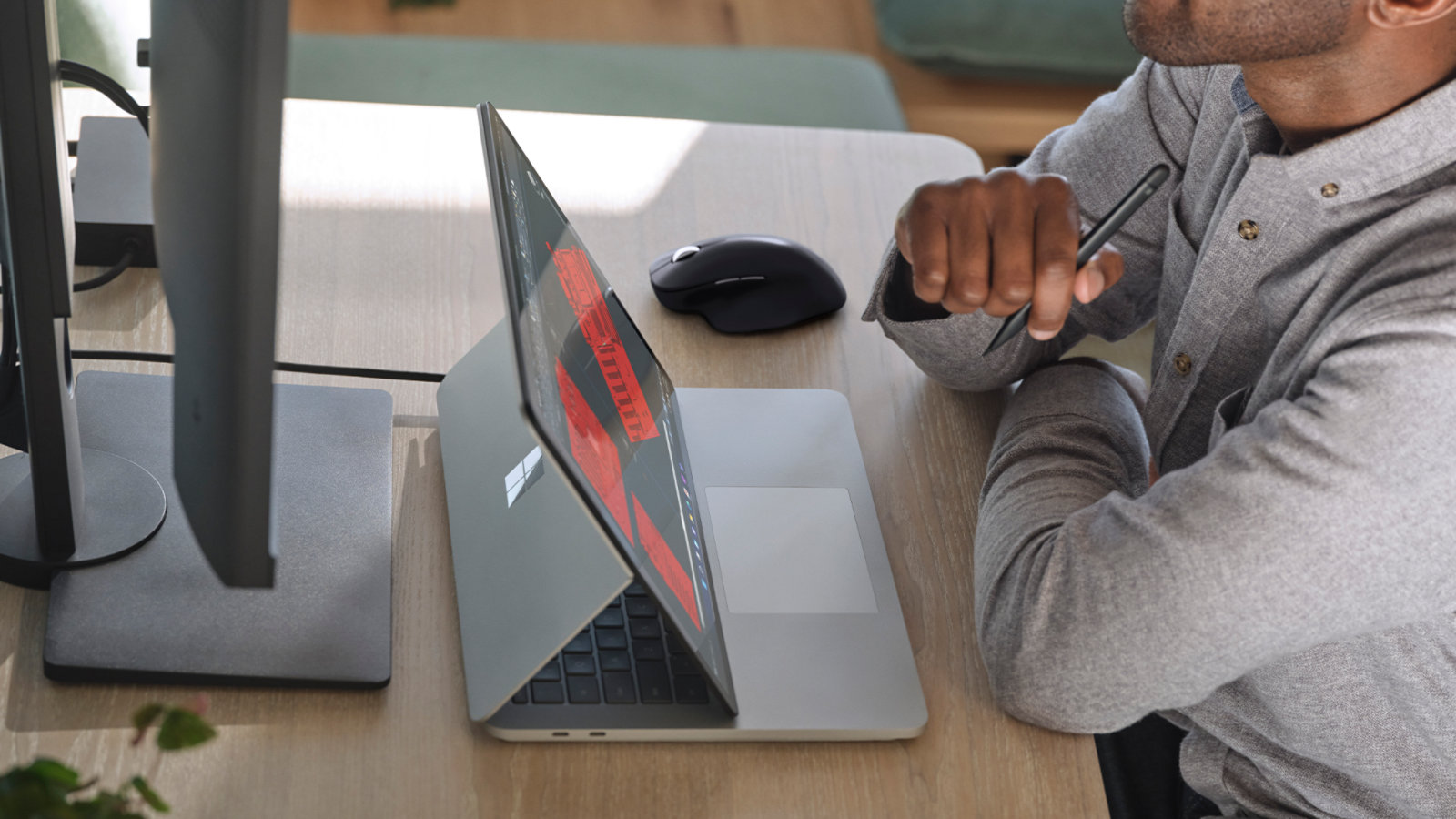 机に座り、法人向け Surface スリム ペン 2 を持って、法人向け Surface Laptop Studio で作業をしている人物。