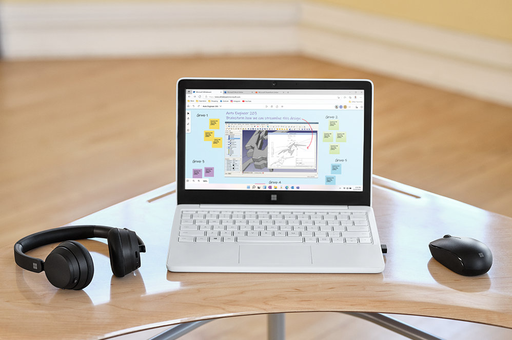 Surface Laptop SE on a desk beside headphones and a mouse.