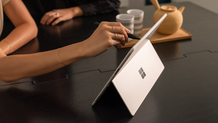 A person’s hand holding Surface Slim Pen 2 for Business writing on the screen of a Surface device.