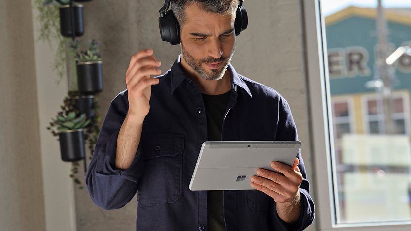 An executive holding a Surface Go 3 in tablet position while wearing Surface Headphones.
