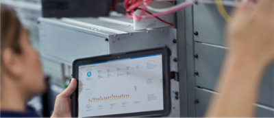 Person holding a tablet with charts in front of a server rack.