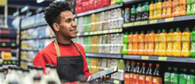 An stock clerk is using a tablet and looking at the shelves.