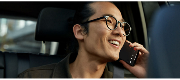A person inside a car, wearing glasses and talking on a phone 
