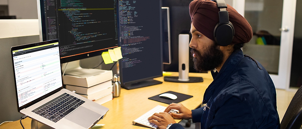 Un uomo che indossa delle cuffie e un turbante e siede a una scrivania con un computer.
