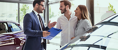 A man and woman talking to a car dealer in a showroom.