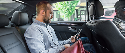 Ein Mann, der auf dem Rücksitz eines Autos sitzt und auf sein Smartphone schaut.