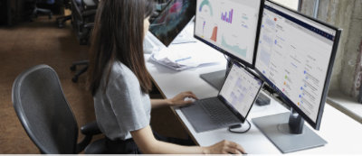Una mujer sentada en un escritorio con dos monitores frente a ella.