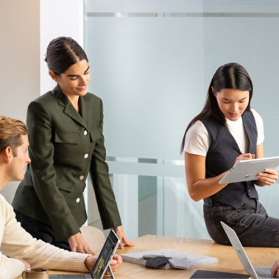 Team members collaborating around a table, with one person taking notes on a tablet during a meeting.
