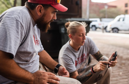 Two people in Team Rubicon shirts look at a smartphone.