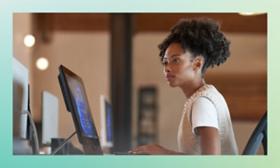 A woman sits at a desk, focused on her computer screen. 