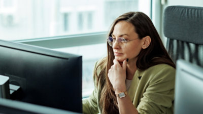 A woman with her hand on her chin looking at a computer screen.