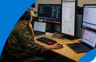 A person working at a desk with two laptops and multiple monitors displaying network information and code.