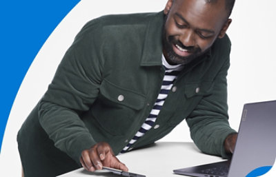 En person læner sig over et bord og bruger en mobiltelefon og en bærbar computer