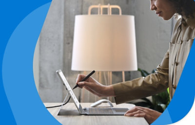 Человек стоит у стола, работая на планшете с помощью пера.