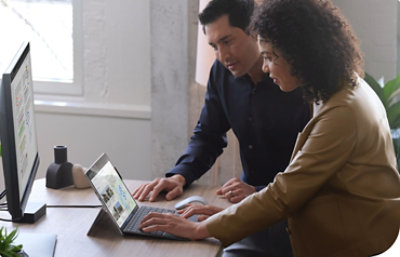 Two people leaning over a desk looking at a Surface device connected to a desktop monitor