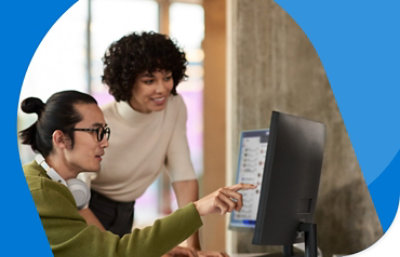 Сотрудник сидит за столом, показывая коллеге, склонившемуся над плечом, информацию на мониторе.