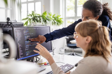 Zwei Personen, die gemeinsam an einem Schreibtisch mit einem Desktopmonitor arbeiten