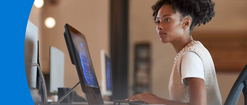 Seorang perempuan muda bekerja dengan sungguh-sungguh di meja dengan monitor komputer ganda dalam pengaturan kantor.