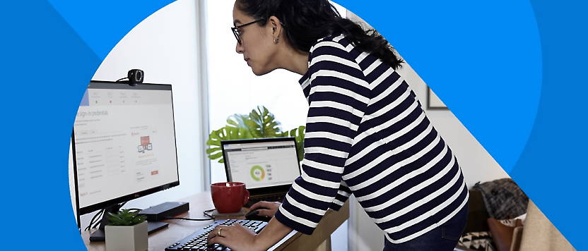 Een vrouw in een gestreept shirt dat aan een bureau werkt met twee computermonitors, typend op een toetsenbord.