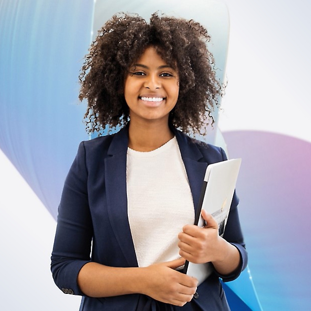 A cheerful young woman with curly hair, holding a laptop, stands in front of a soft blue background 