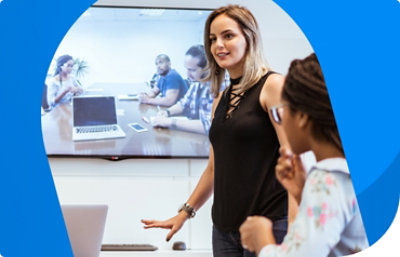 Dos personas en una sala de conferencias en la que se muestra una videollamada en una pantalla grande que tienen detrás.