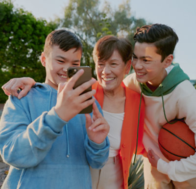 屋外でスマートフォンを見ながら微笑む 2 人のティーンエイジャーと年配の女性。