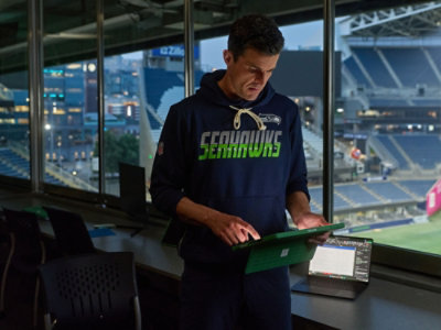 Person wearing a navy-blue Seattle Seahawks hoodie and looking at a tablet device