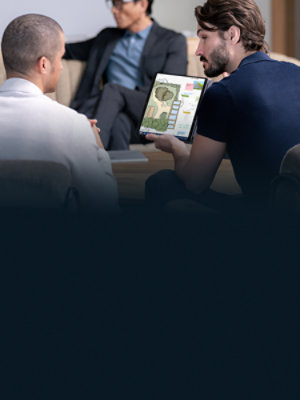 A man holding a black Surface Pro 10 while speaking to another person during a meeting. 