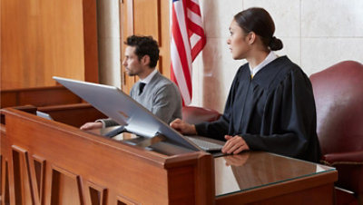 A judge and a colleague sitting at their desk in front of a large computer
