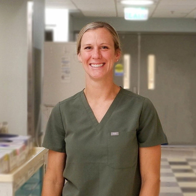 Female standing in a medical center wearing green scrubs.