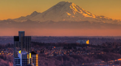 A city skyline at sunset with Mount Rainier in the background.