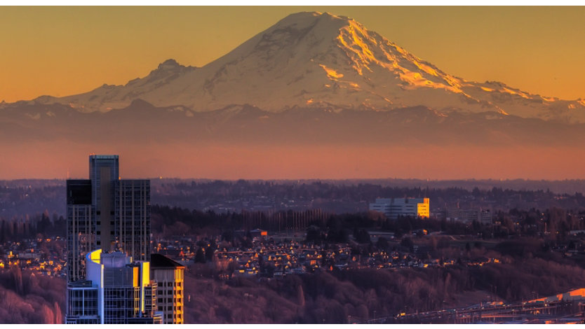 A city skyline at sunset with Mount Rainier in the background.