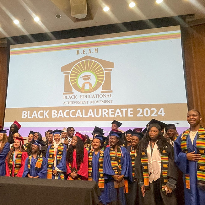 A group of graduates in caps and gowns posing on stage at a "Black Baccalaureate 2024" event.