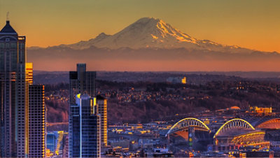 A city skyline at sunset with Mount Rainier in the background.