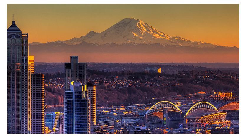 A city skyline at sunset with Mount Rainier in the background.