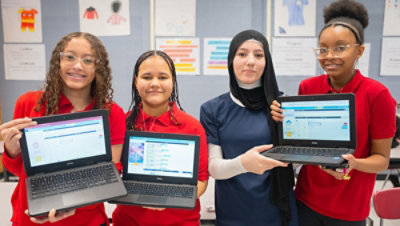 Four people holding laptops showing screens in a classroom.