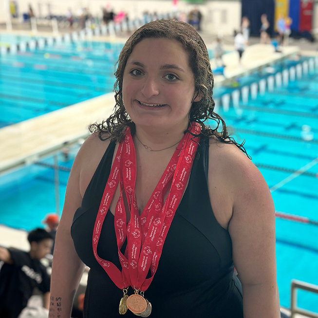 Female swimmer standing out of the pool wearing medals.