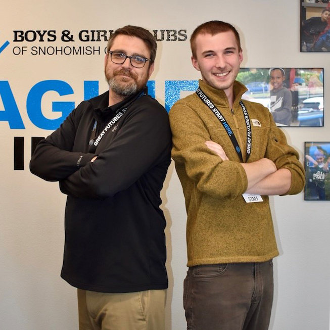 Robert and Brandon, two men standing side by side; back-to-back smiling with their arms crossed.