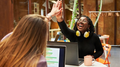 Two people high-fiving at a table with laptops and coffee mugs.