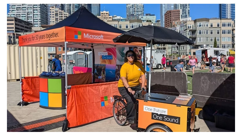 A woman with a tricycle cart at an outdoor event, with city buildings in the background.