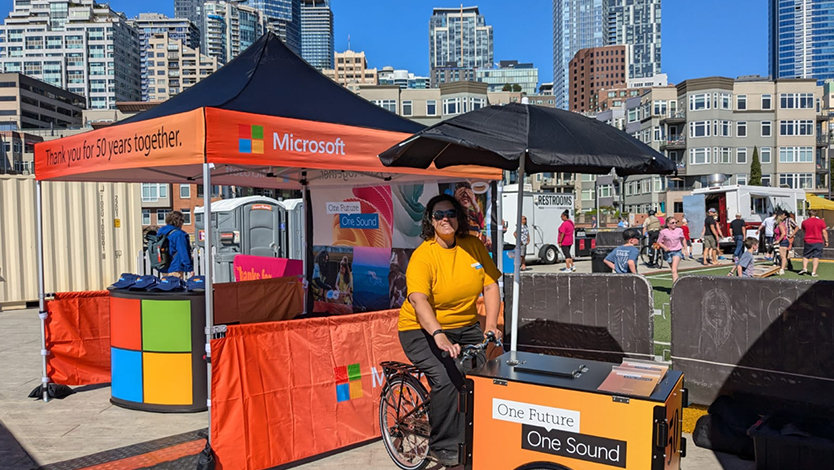 A woman with a tricycle cart at an outdoor event, with city buildings in the background.