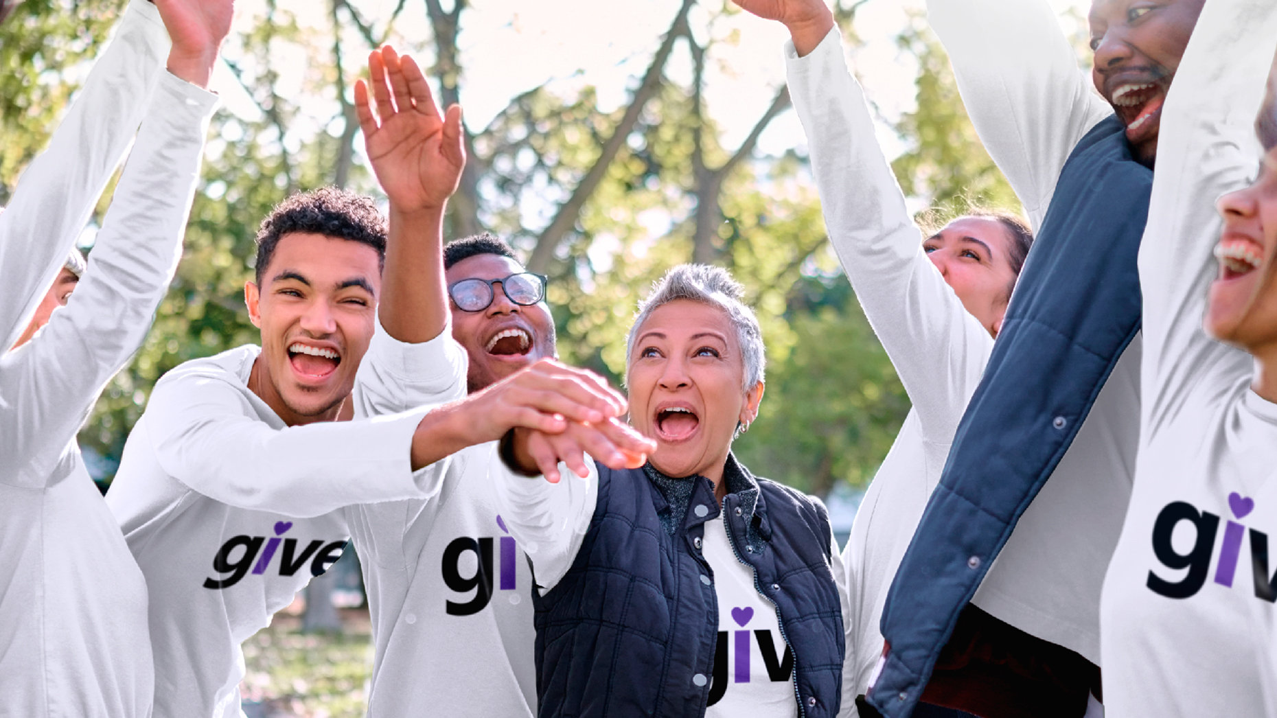 People outdoors in white “give” t-shirts celebrating with their hands in the air.