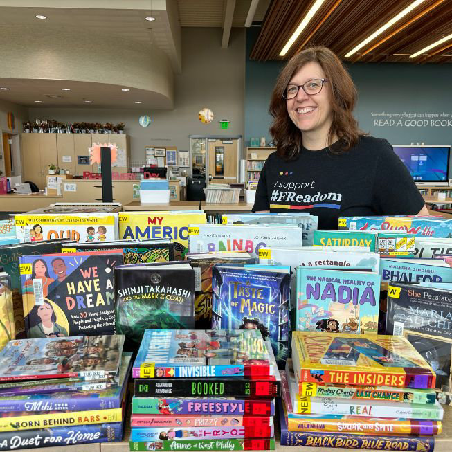 Lake Washington school female volunteer standing behind stack of books smiling.