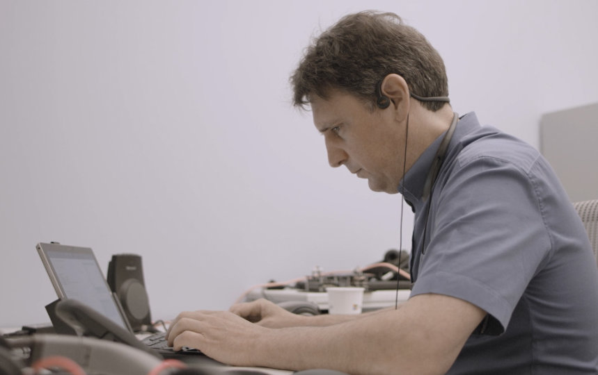 Amos Miller works on his computer while wearing bone conducting headphones