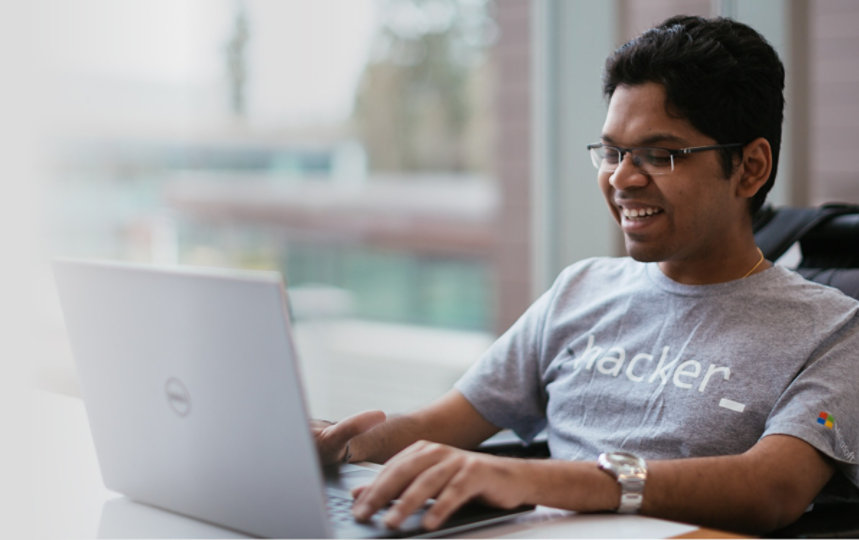A man in a wheelchair and wearing a shirt that says hacker smiles as he types on his computer