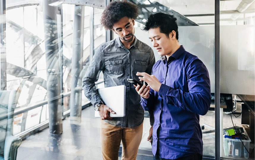 Two colleagues looking at a smartphone while working together in an office. 