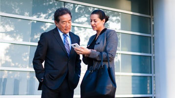 Business man and lady standing in courtyard while looking at a cell phone