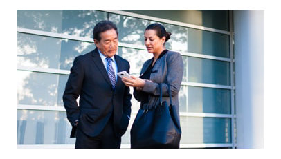 Business man and lady standing in courtyard while looking at a cell phone