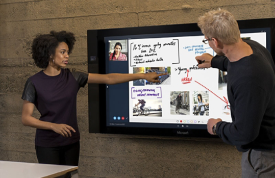 Man and woman presenting in front of a large touchscreen